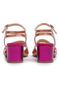 Sandalen in bronzetönen mit offenem Rücken, ausgestattet mit zwei verstellbaren Riemen und einem rosa blockartigen Absatz mit rissiger Textur.
