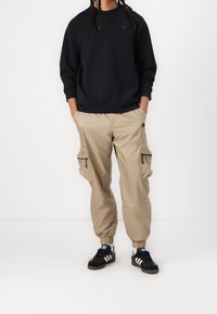 Černá mikina, béžové cargo kalhoty s bočními zipy a černé tenisky s bílými pruhy. Pohodlný, volný střih s elastickými manžetami.