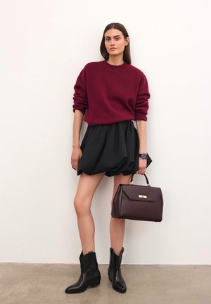 Pulover tricotat burgund, fustă voluminoasă neagră, cizme din piele neagră până la gleznă și o geantă de umăr maro închis cu accesorii aurii. Design minimalist.