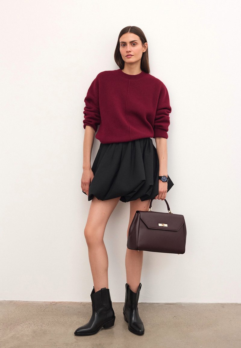 Burgundowa dzianinowa bluza, czarna objętościowa spódnica, czarne skórzane botki za kostkę oraz ciemnobrązowa torebka z złotymi akcentami. Minimalistyczny design.