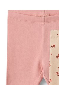 Detailní záběr na růžové žebrované kalhoty látky s béžovou záplatou a malými červenými květinovými motivy na pravé straně.