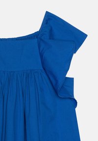 Sininen kangas, jossa on teksturoitu pinta, ja kerätty pääntie sekä rypytetty hihasuunnittelu. Materiaali vaikuttaa kevyeltä ja hengittävältä.