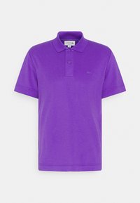 Polo de color púrpura hecho de una tela suave, con un cierre de dos botones, mangas cortas y un pequeño logo de Lacoste en el pecho.