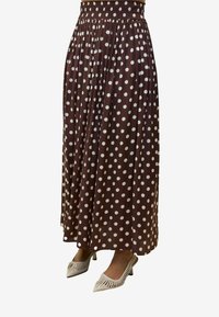 Gonna maxi plissettata a pois marroni con vita smock, abbinata a scarpe bianche a punta con dettagli cut-out.
