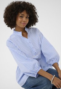 Bluză cu dungi albastre și albe, guler tip tunică, deschidere cu nasturi pe jumătate și mâneci bufante. Are un detaliu delicat din dantelă de-a lungul părții frontale.