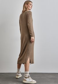 Braunes geripptes Strickkleid mit langen Ärmeln und Seitenschlitzen. Kombiniert mit beigen Sneakers und hellen Crew-Socken. Schlichtes Design.