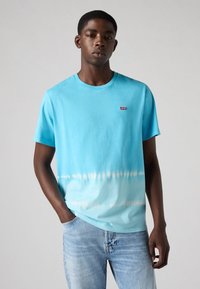 Lichtblauw katoenen T-shirt met een geleidelijke witte tie-dye-effect aan de onderkant. Bevat een klein rood Levi's-logo op de borst.