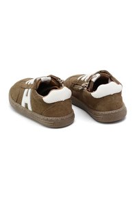 Zapatillas de ante marrón con detalles en blanco, suela texturizada y cordones. Forma redondeada con un detalle en el talón curvado.