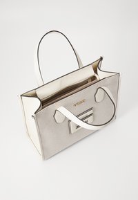 Grå canvas tote-väska med vita läderdetaljer, guld "GUESS"-logotyp, två handtag högst upp och en innerficka med dragkedja. Öppen design.