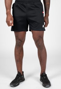 Zwarte sportshorts met een elastische tailleband, zijzak en witte logo-accent. De stof is glad en lichtgewicht.