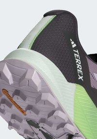 Scarpa sportiva nera e grigia con dettagli verdi. Upper testurizzato con logo di marca visibile. Suola in gomma con battistrada viola e arancione.