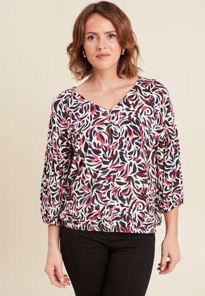 Bloemmotief blouse in wit, rood en marineblauw. V-hals, 3/4 pofmouwen en elastische zoom voor een ontspannen pasvorm. Gepaarde met zwarte broeken.