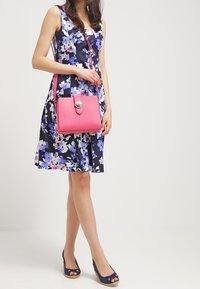 Vestido navy con estampado floral y acentos en púrpura y rosa, acompañado de un bolso cruzado rosa con un cierre plateado y zapatos navy.