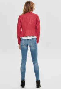 Veste en cuir rouge avec des épaules texturées, design ajusté, ourlet incurvé, et jean skinny bleu clair, accompagnés de bottines noires.