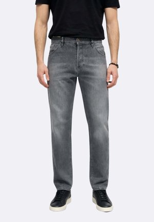 Uomo che indossa jeans grigi sbiaditi a gamba dritta, sneakers nere con suole bianche e una maglietta nera a maniche corte, in piedi con le braccia rilassate.