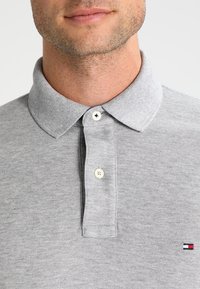 Grå polo skjorte med kravehals, to-knap lukning, struktureret stof og lille logo mærke på venstre bryst.