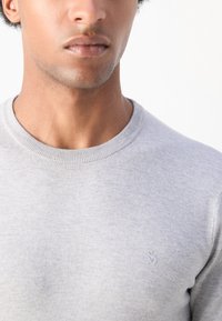Gray crew neck sweater made of soft fabric with a subtle texture. Features a small embroidered logo on the left chest area.