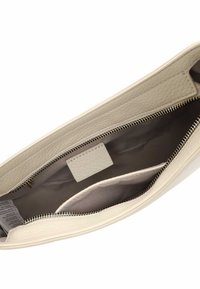 Cremfarbende Leder-Clutch mit Reißverschluss, die eine glatte Textur und ein Stofffutter aufweist. Das Innere beinhaltet eine kleine Tasche und ein Etikett.