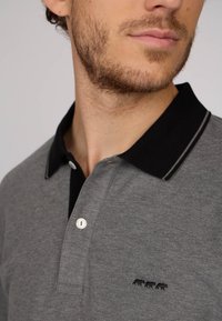 Polo gris avec un col noir, comportant un bouton blanc et un petit motif brodé de trois ours près de l'ourlet.