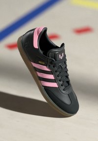 Sort atletiksko med pink accenter og tre sorte striber. Har en struktureret overdel, snøredesign og en sål af gummigummi.