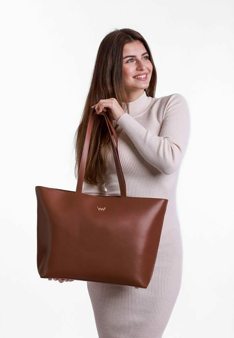 Hnědá kožená taška přes rameno s elegantním, minimalistickým designem; vybavená pevným uchem a zlatým logem na přední straně. Hladká textura.