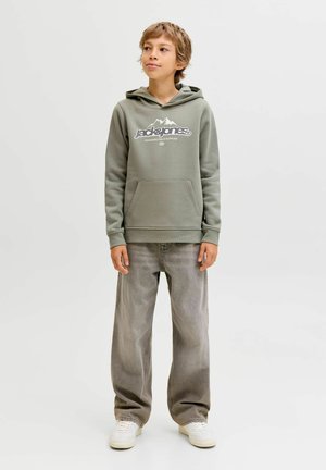 Žalias gobtuvas su balta kalno grafika ir prekės ženklu, priekinė kišenė, derinamas su šviesiai pilkomis plačiomis kelnėmis ir baltomis sportbačiais.