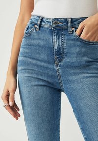 Blå denim högmidjade jeans med fem fickor, knäppning fram och kopparstickningar. Slät textur med lätt blekning.