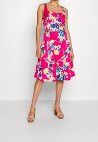 Blommönstrad ärmlös klänning i stark rosa, med blå, gula och lila detaljer. Knälång med en figursydd midja och utsvängd kjol.