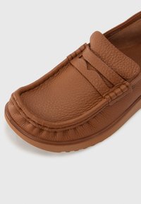 Brūni ādas slip-on zābaki ar teksturētu virsmu, mokasīnu stila šuvu un gludu gumijas zoli. Iekļauti smalki dekoratīvi akcenti.