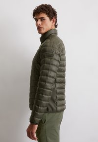 Kurtka pikowana w kolorze oliwkowym, z poziomymi przeszyciami, wysokim kołnierzem oraz kontrastowym, dopasowanym bocznym panelem.