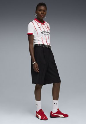 Vit kortärmad skjorta med röda ränder och krage, svarta plisserade shorts, svart och vit bälte, röda sneakers och vita strumpor med logotyper.