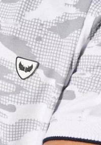 Witte shirt met een grijs camouflagepatroon, voorzien van een driehoekig embleem met een gestructureerd oppervlak en een donkere rand op de linker schouder.