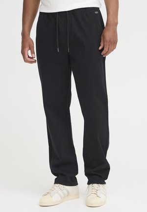Black jogger pants in a relaxed fit, made of soft material with an elastic waistband and drawstring. Features side pockets and subtle branding.
