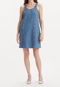 Denimklänning utan ärmar med justerbara band, sidoknappar och rak skärning. Ljusblå färg, avslappnad design med synliga sömdetaljer.