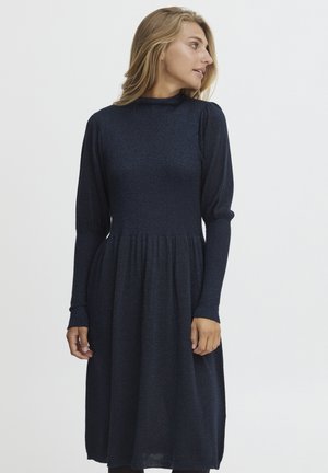 Navyblaues Kleid mit hohem Kragen, langen Ärmeln, strukturiertem Stoff und ausgestellt Rock. Verfügt über ein tailliertes Oberteil und eine gefaltete Taille.