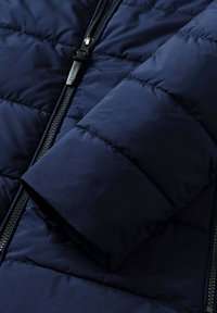 Chaqueta acolchada azul marino con diseño acolchado, equipada con una cremallera resistente y un acabado liso y mate en la tela. Destacada por las mangas acolchadas.