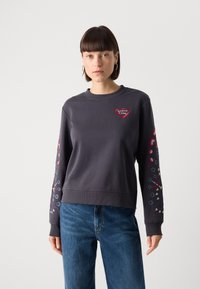 Felpa grigia con scollo rotondo, caratterizzata da logo a cuore rosso e dettagli colorati sulle maniche. Realizzata in tessuto morbido, vestibilità rilassata.