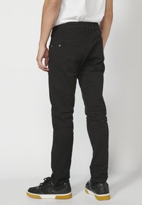 Fekete, slim-fit farmernadrág texturált felülettel, hátsó zsebekkel és diszkrét varrási részletekkel, fekete sportcipőkkel és fehér inggel párosítva.