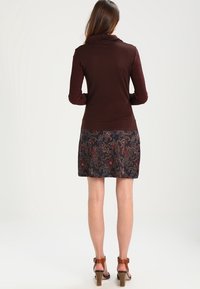 Haut à manches longues marron avec des manches texturées et une jupe sombre à motifs floraux. Des sandales à talons marron complètent la tenue.