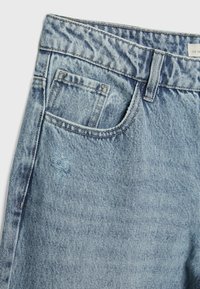 Jean en denim bleu clair avec un délavage naturel, un design standard à cinq poches et une petite zone usée sur le devant.