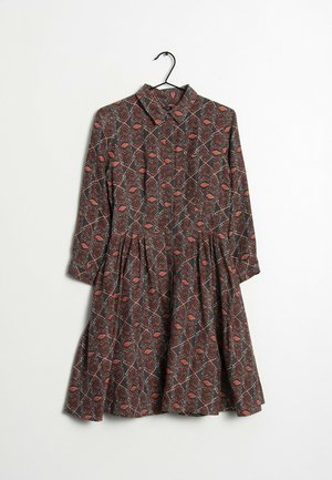 Tiskované šaty s dlouhými rukávy, límečkovým výstřihem a rozšířenou sukní. Mají tmavé pozadí s geometrickými červenými a bílými vzory.