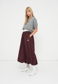 Sweatshirt cinza curto com logótipo preto, combinado com calças largas bordô com bolsos laterais, e sapatos brancos. Textura suave no geral.
