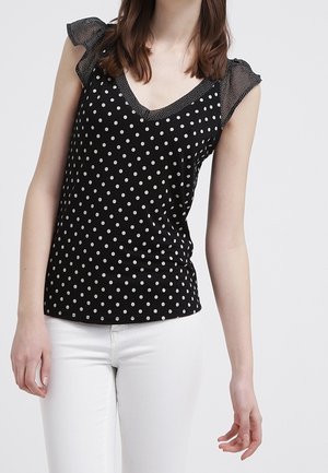 Haut noir sans manches à pois blancs, avec un col en V et des accents de mesh volantés sur les épaules. Tissu doux et ajusté.