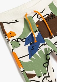 Close-up van kinderbroekjes met kleurrijke dinosaurusthema's en oranje koordjes op een witte geribbelde tailleband.