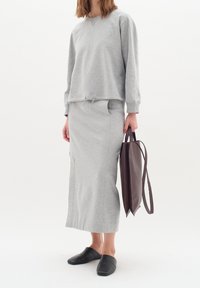 Sudadera gris de mezcla de algodón con mangas largas, falda midi gris a juego y zapatos negros sin cordones. La modelo sostiene un bolso tote marrón oscuro.