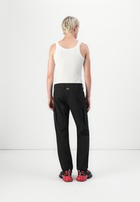 Zwarte cargobroek met zakken aan de zijkanten, gecombineerd met een witte geribbelde tanktop. De schoenen zijn zwart met rode accenten en een chunky zool.