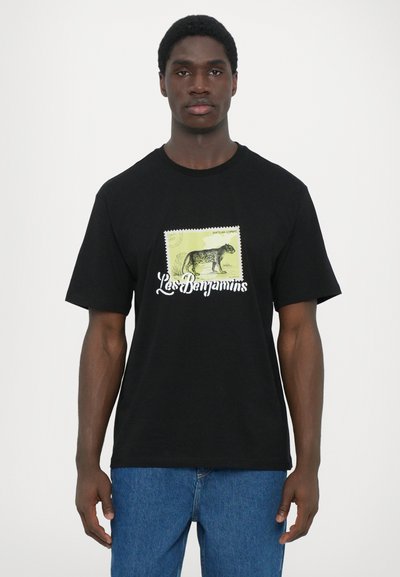 T-shirt en coton noir avec un design d'estampille vert et jaune, comprenant une illustration de chien et le texte "Les Benjamins" en blanc. Manches courtes.