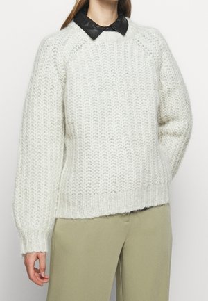 Stevige gebreide crèmekleurige trui met een gestructureerde afwerking, voorzien van een zwarte leren kraag en geribbelde manchetten, gecombineerd met lichtgroene broek.