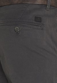 Calças de algodão cinza-escuras com fecho de botão, bolso traseiro e um pequeno logótipo junto à cintura. Textura suave.