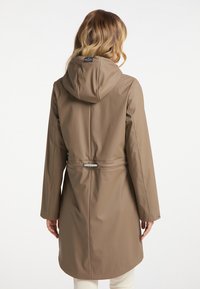 Beige waterproof raincoat with a hood, adjustable drawstring waist, long sleeves, and a smooth texture, featuring a back yoke and minimal hardware.